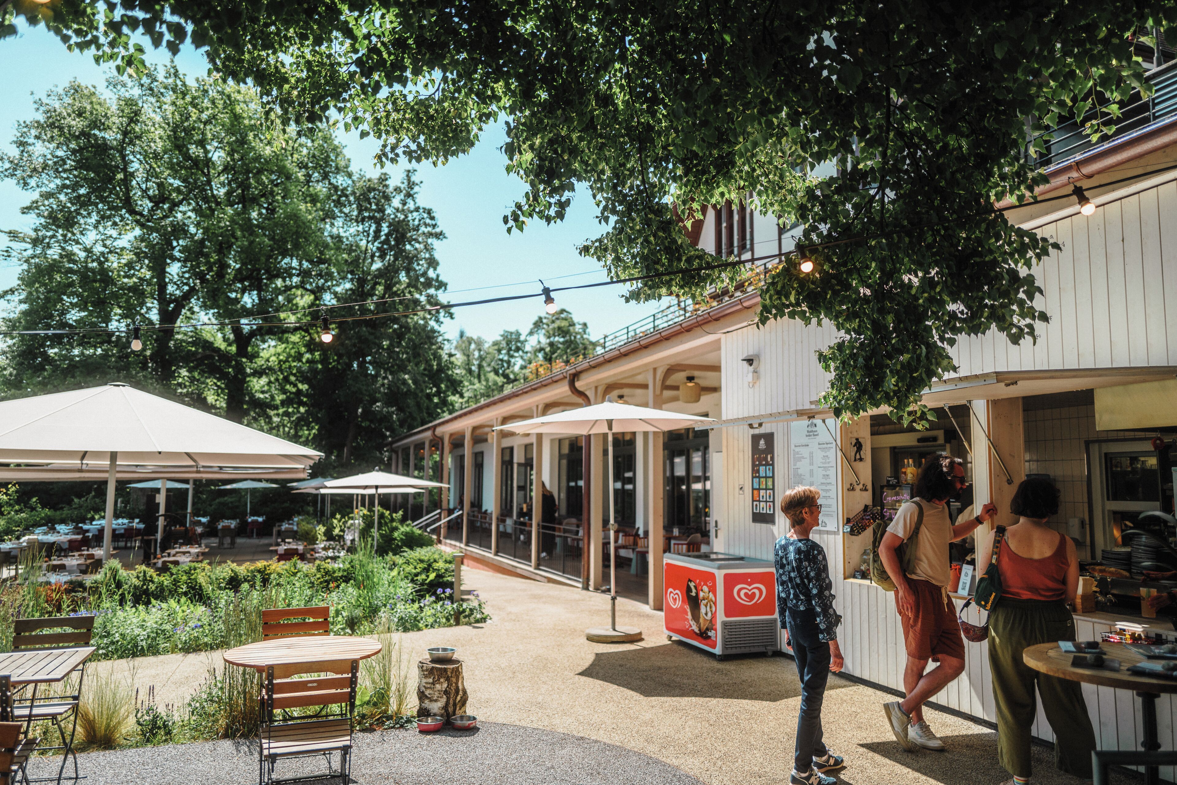 Un espace extérieur aménagé pour les repas, avec des tables et des chaises, entouré de verdure et d’arbres.