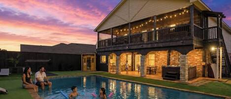Une maison à deux étages avec une piscine, un espace salon extérieur et des guirlandes lumineuses.