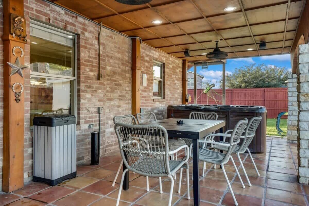 An outdoor patio with a brick wall, a grill, and a table with chairs.