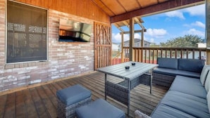 En udendørs terrasse med murstensvæg, fladskærms-tv, fletmøbler og træterrasse.