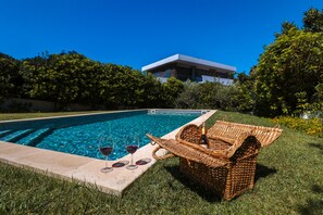 Una piscina con una sedia in vimini e bicchieri da vino sul bordo.