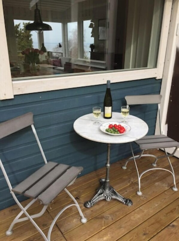 A small outdoor seating area with a round table, two chairs, a bottle of wine, and a plate of fruit.