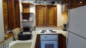 A compact kitchen with wooden cabinets, a white stove, and a sink. - Beautiful, secluded, open plan cottage with spectacular sea views (Castara)