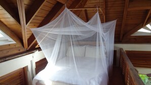A bed with a white canopy in a wooden room with sloped ceilings. - Beautiful, secluded, open plan cottage with spectacular sea views (Castara)