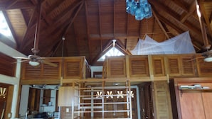 A spacious loft-style room with a high ceiling, wooden beams, and a mezzanine level. - Beautiful, secluded, open plan cottage with spectacular sea views (Castara)