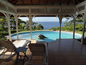 A covered pool area with a view of the ocean, featuring a gazebo, lounge chairs, and a tiled floor. - Beautiful, secluded, open plan cottage with spectacular sea views (Castara)