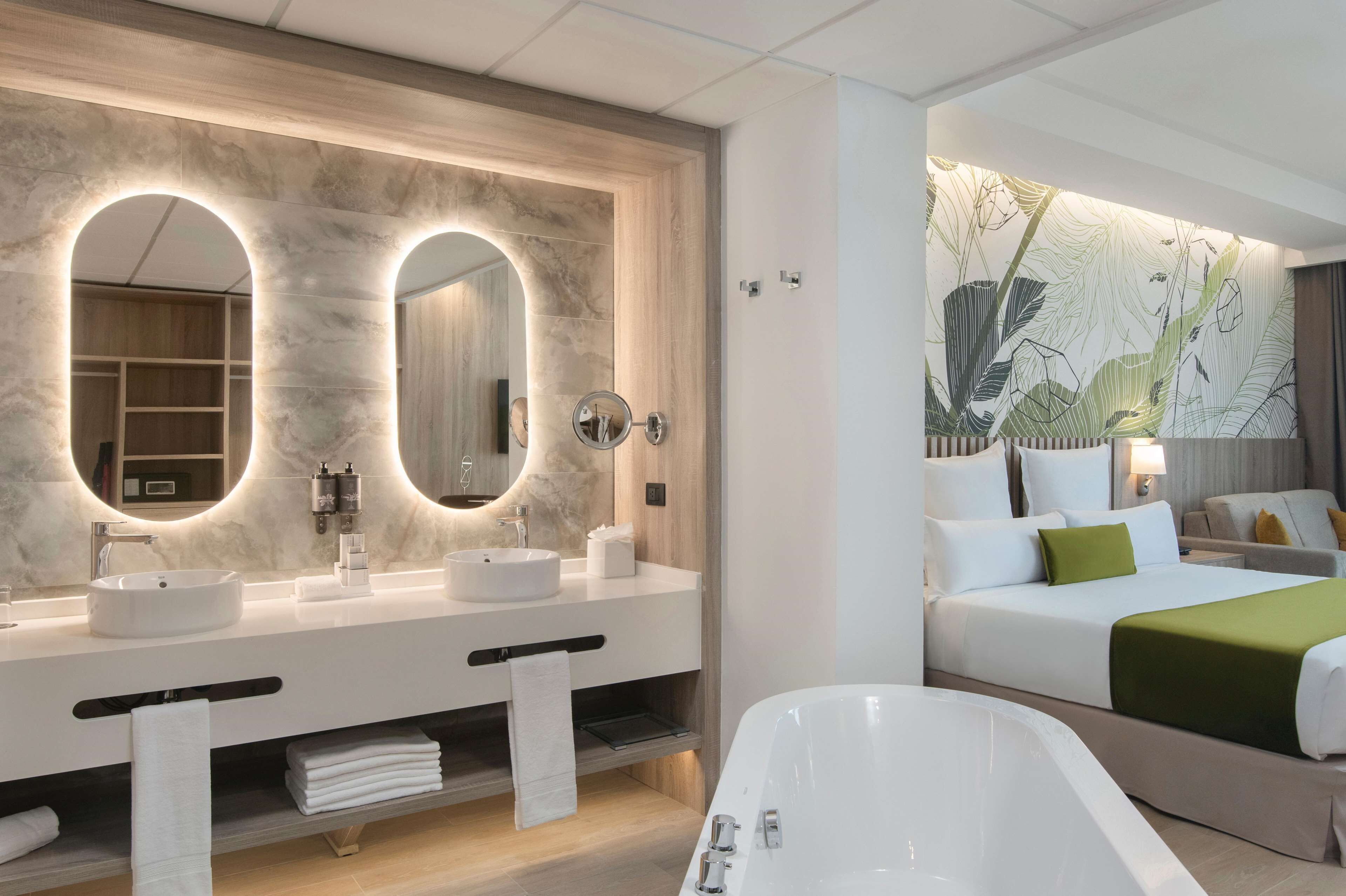A modern bathroom with a large mirror, dual sinks, and a bathtub.