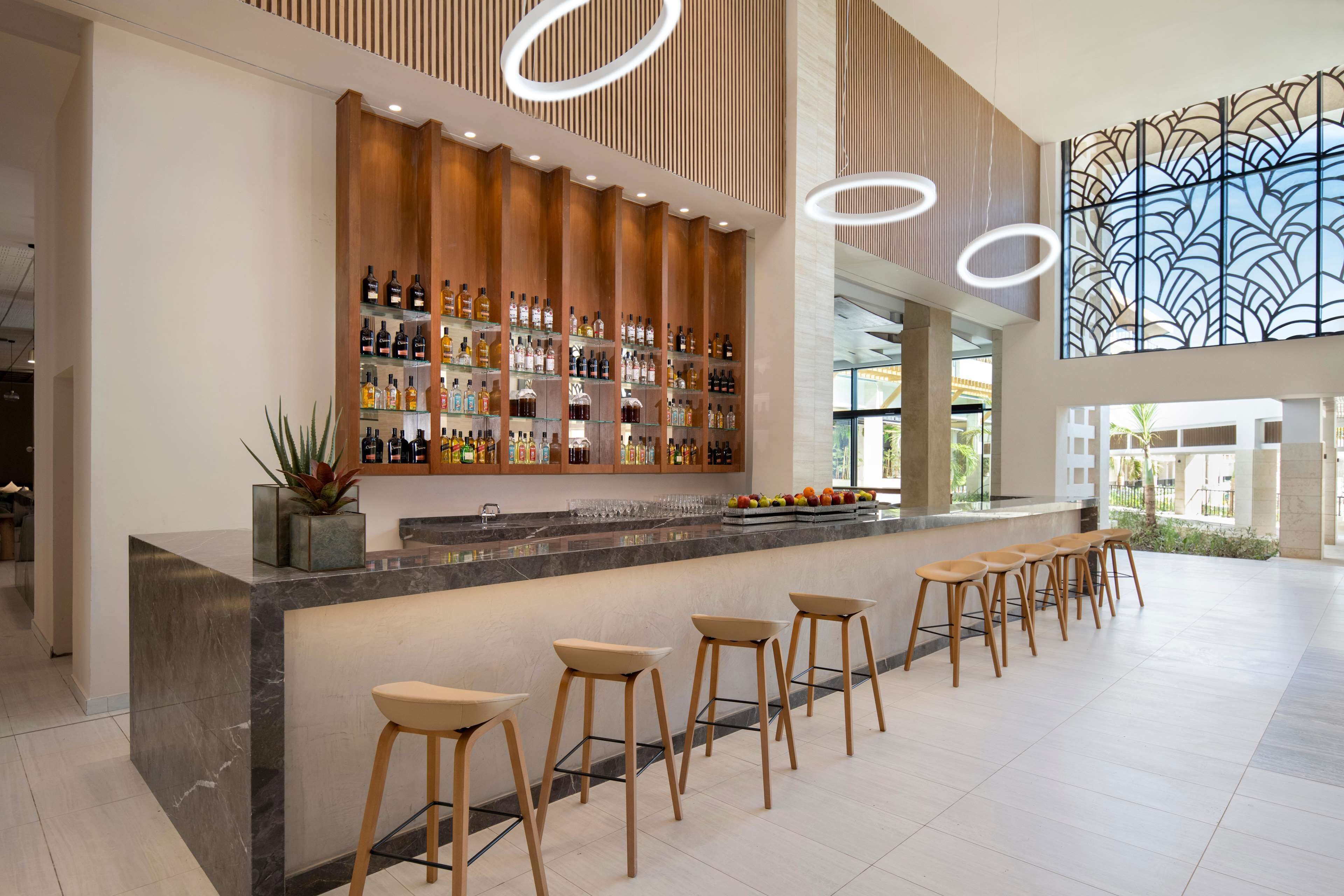 A modern bar area with a long counter, multiple stools, and a variety of bottles.