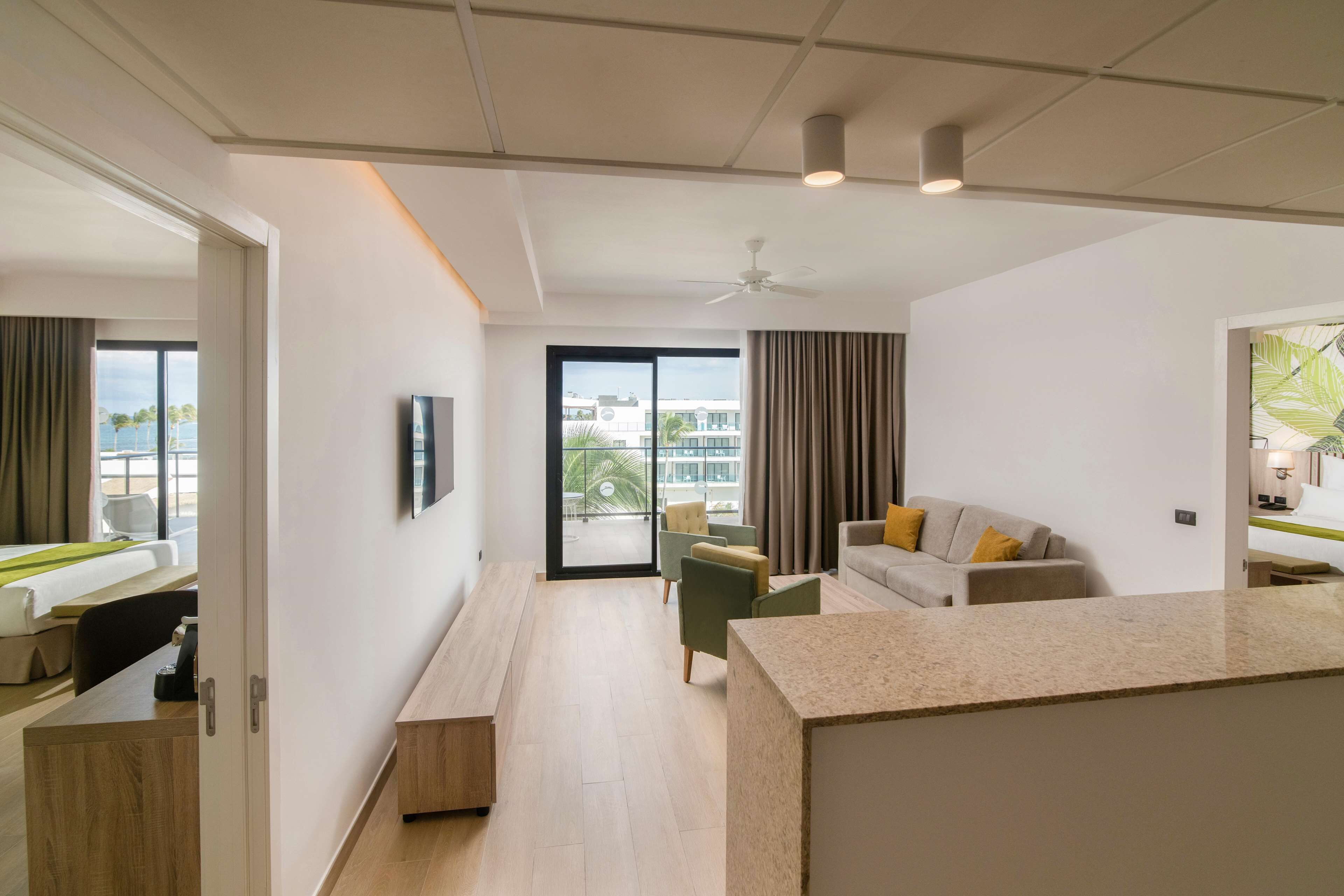A modern hotel room with a balcony, a sofa, a dining area, and a TV.
