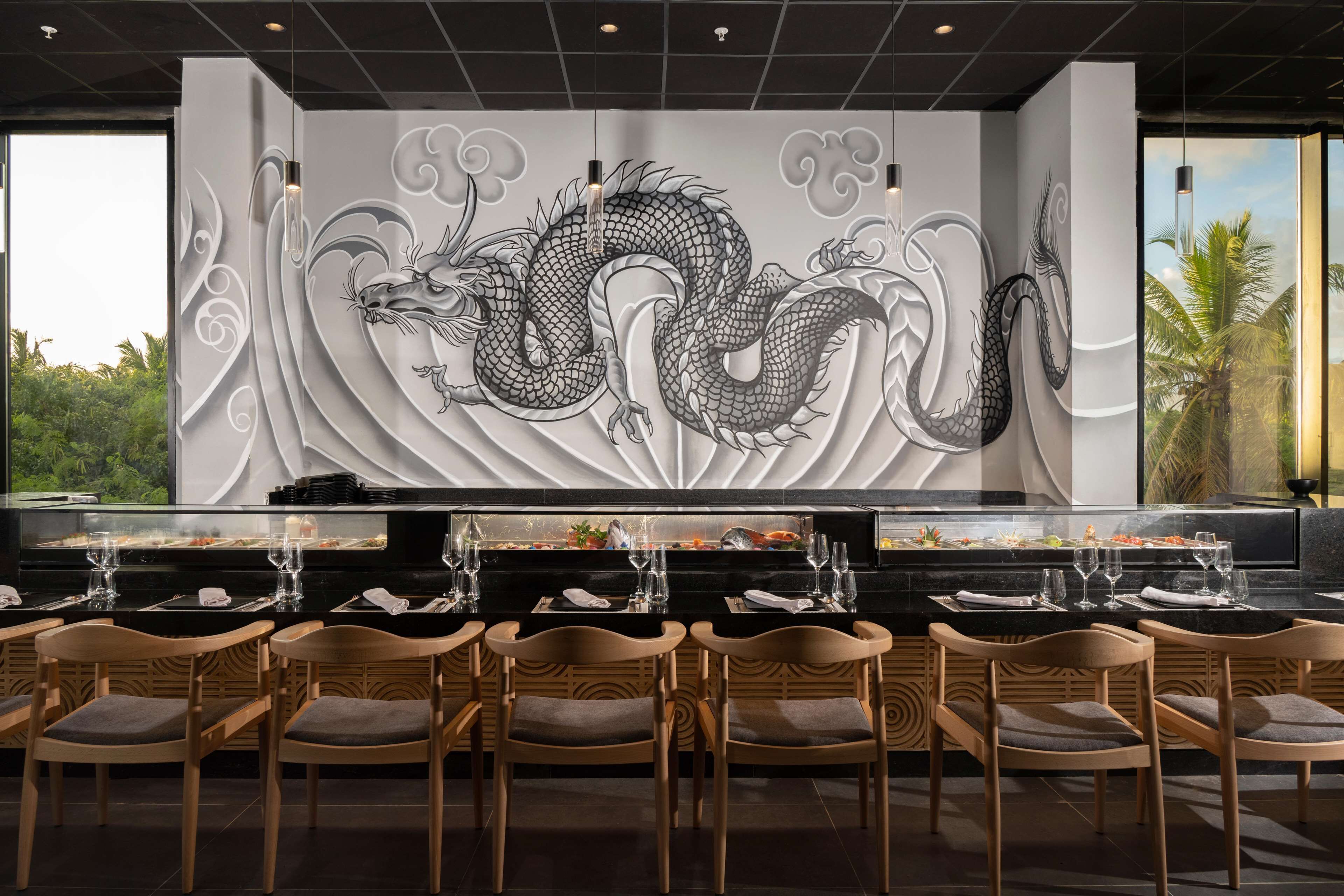 Un restaurante con un mural de dragón, sillas de madera y una encimera negra.