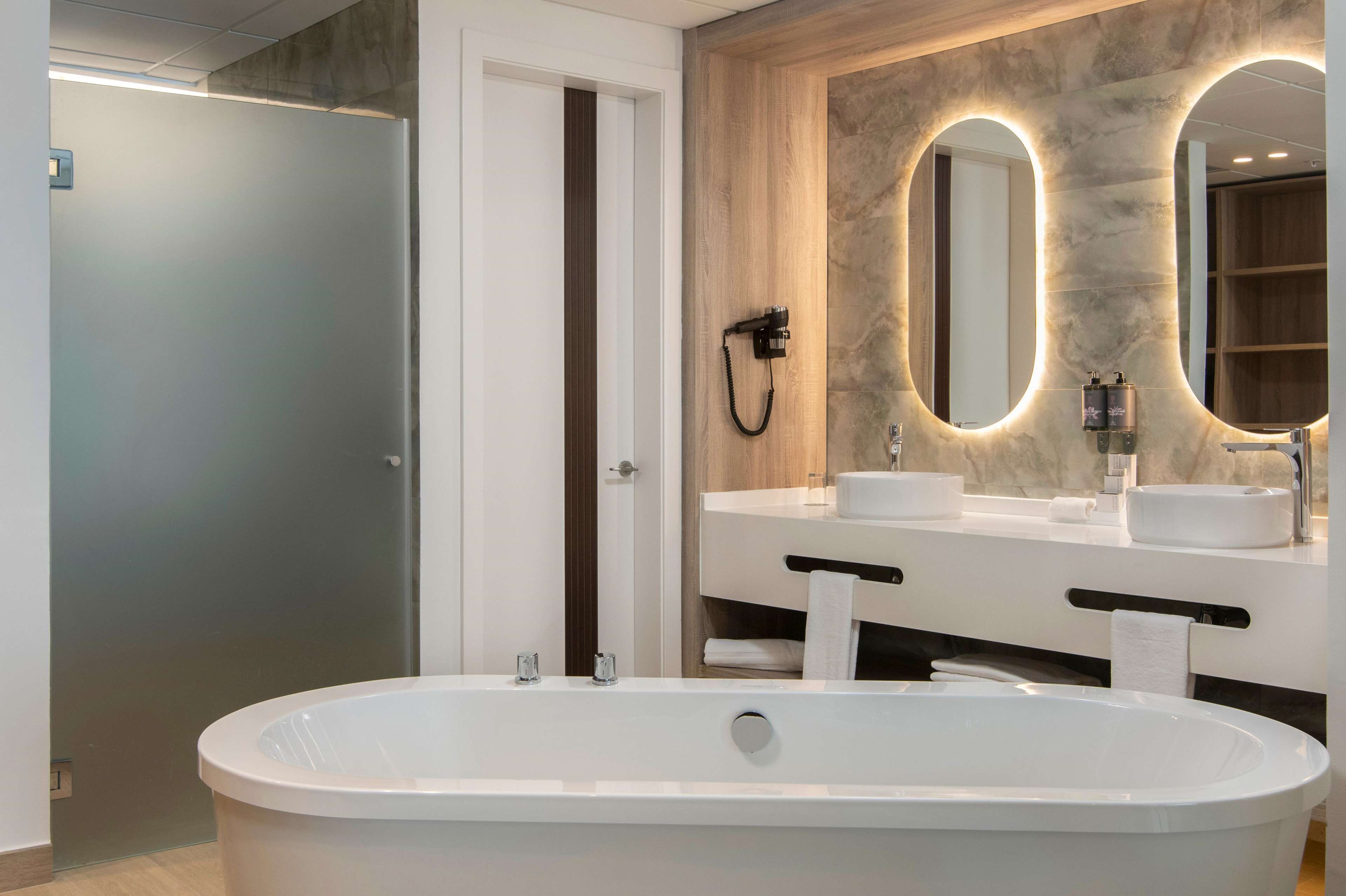 Un baño moderno con una bañera independiente, dos lavamanos y un espejo grande con iluminación integrada.