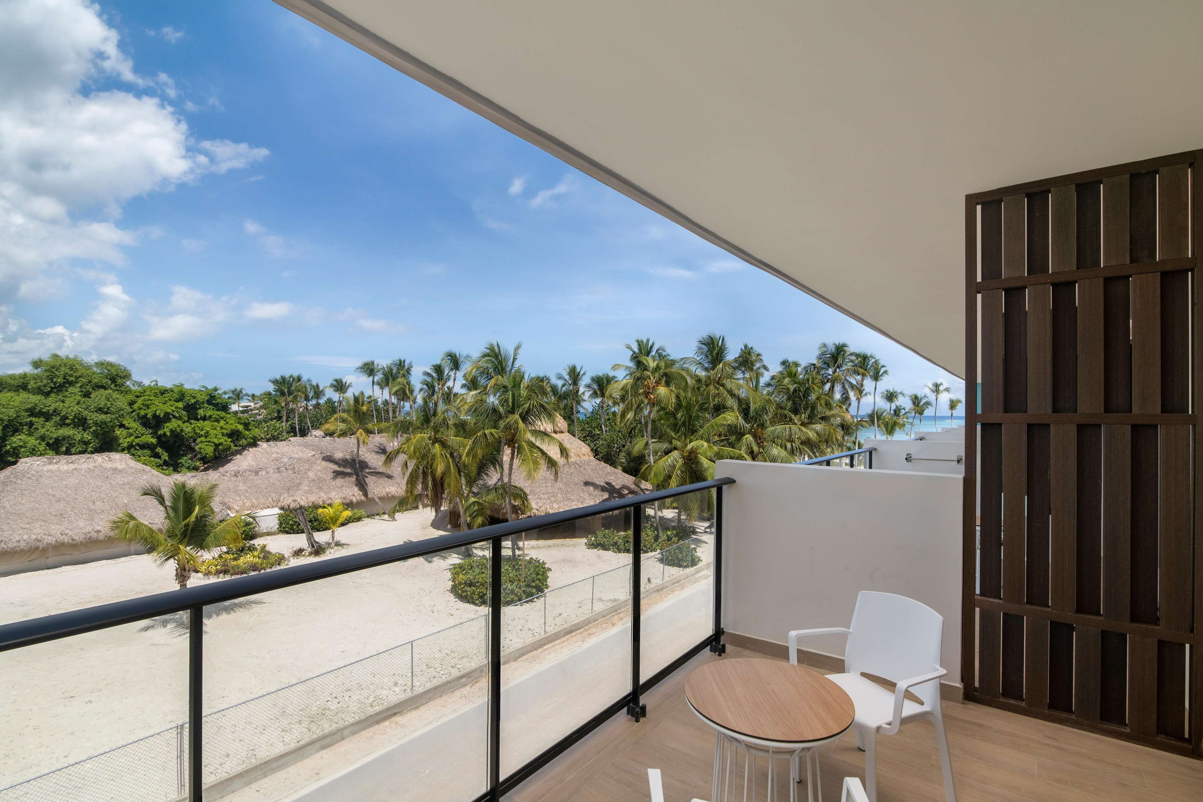 Een balkon met uitzicht op een strand, palmbomen en een heldere lucht.