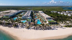 Vista aérea de un complejo turístico con varias piscinas, zonas de playa y una gran cantidad de sillas de playa.