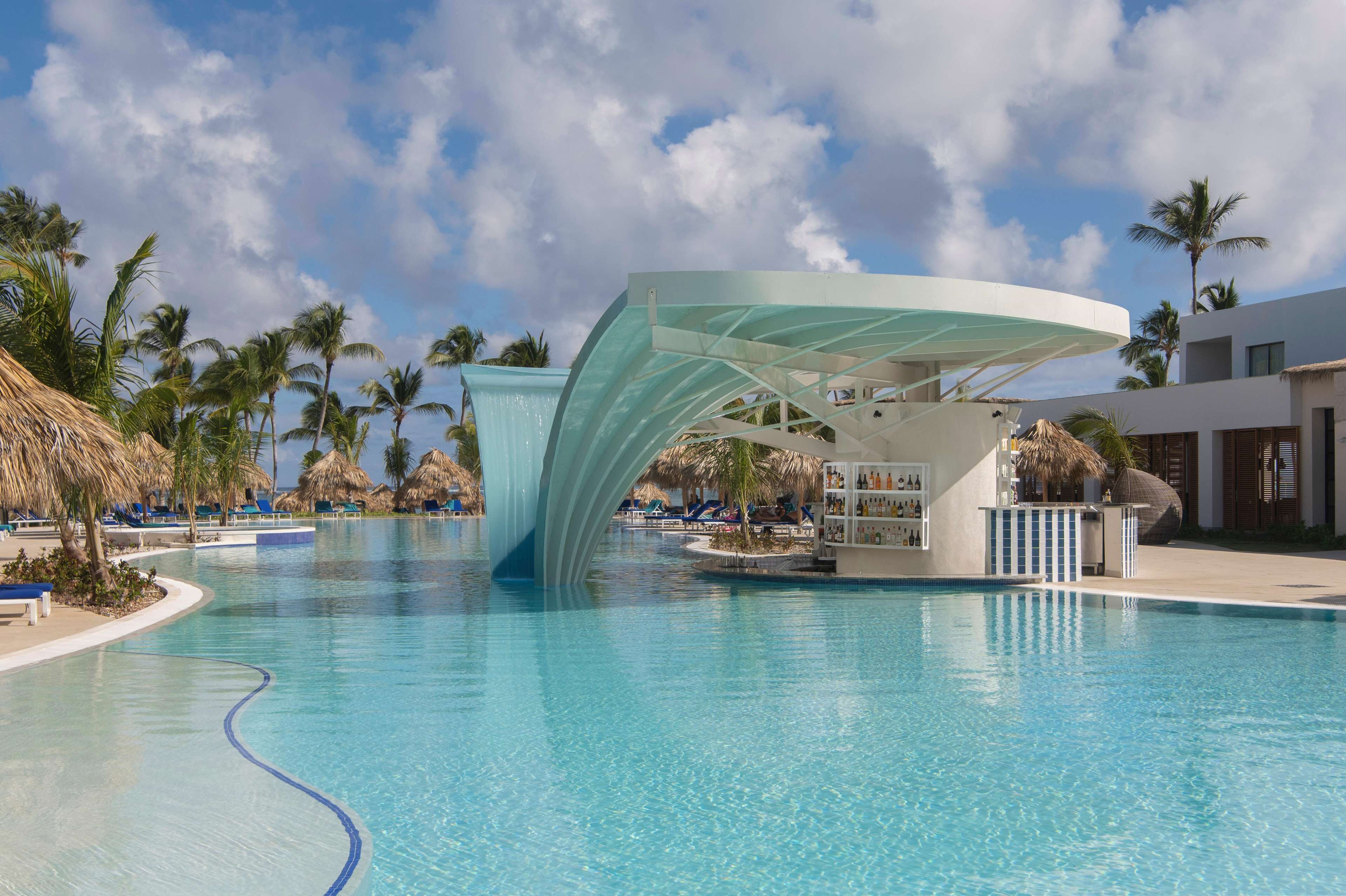 A swimming pool with a modern structure, palm trees, and lounge chairs.