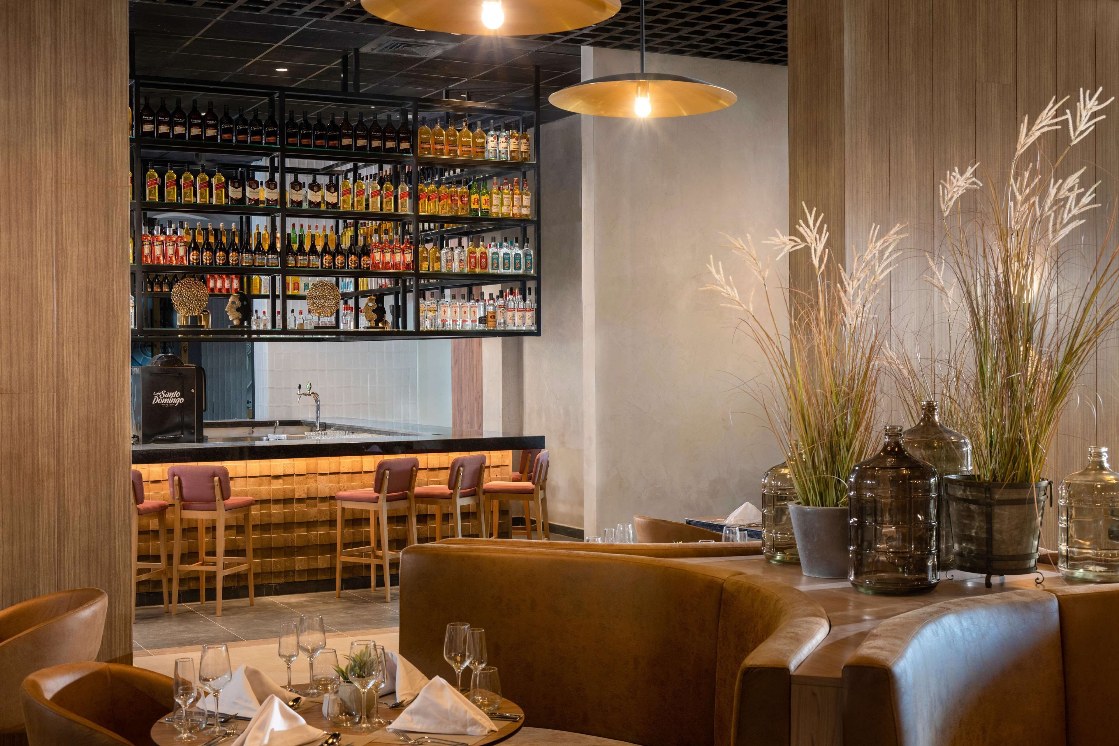 A bar area with shelves of liquor bottles, a bar counter, and seating with a table set for dining.