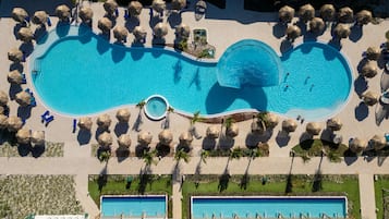 Vista aérea de un resort con una amplia piscina central rodeada de tumbonas y palmeras.