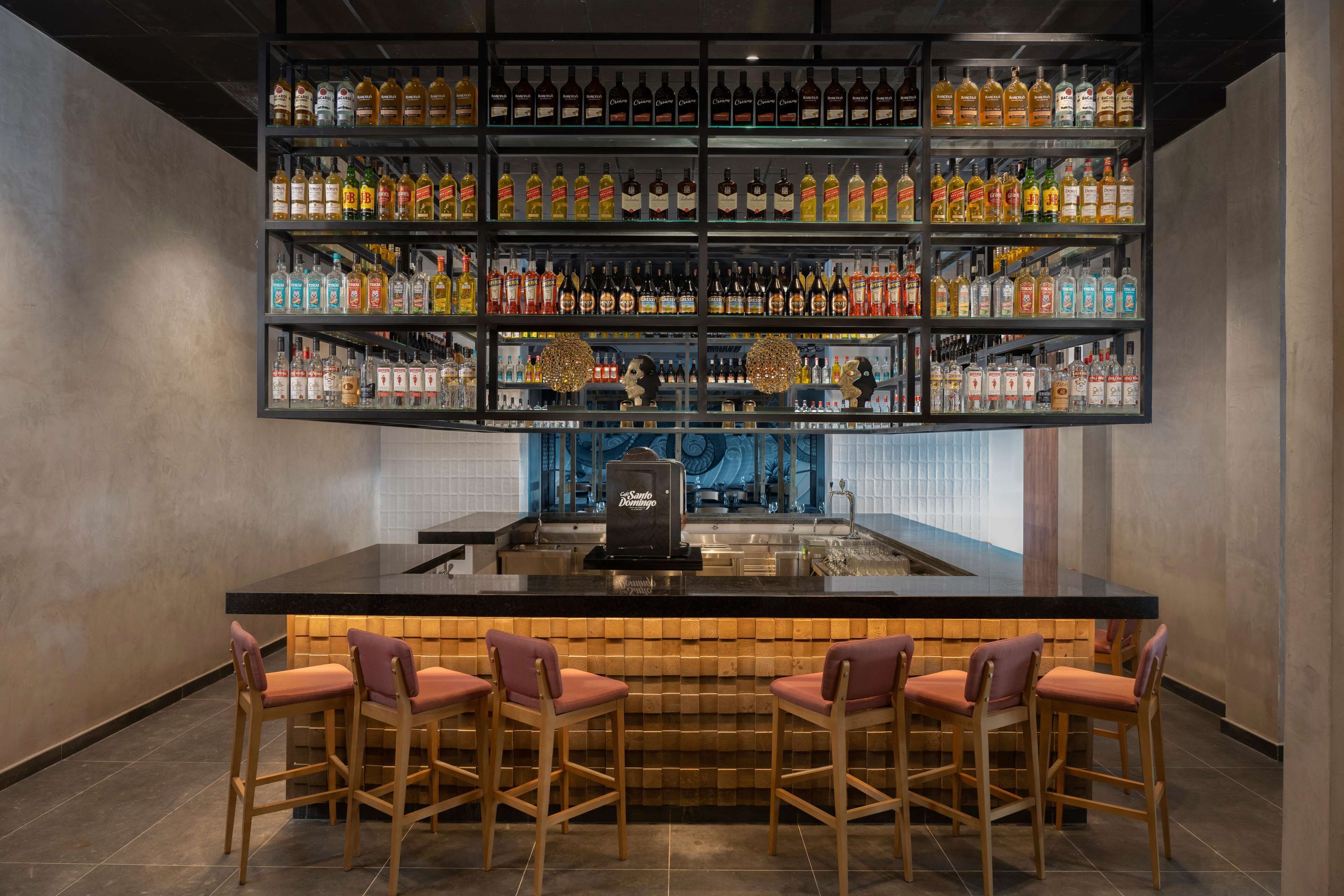 A bar area with multiple shelves of liquor bottles, a central bar counter, and four bar stools.
