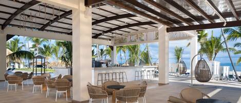 An outdoor patio area with wicker furniture, a bar, and a view of palm trees and the ocean.