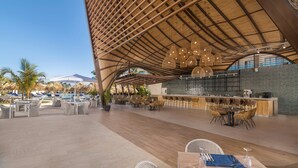 An outdoor dining area with wicker furniture, a bar, and a pool in the background. - Serenade All Suites - Adults Only Resort - All inclusive (Punta Cana)