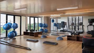 Une salle de sport moderne équipée de matériel d’exercice, dotée de grandes fenêtres et d’un plancher en bois.