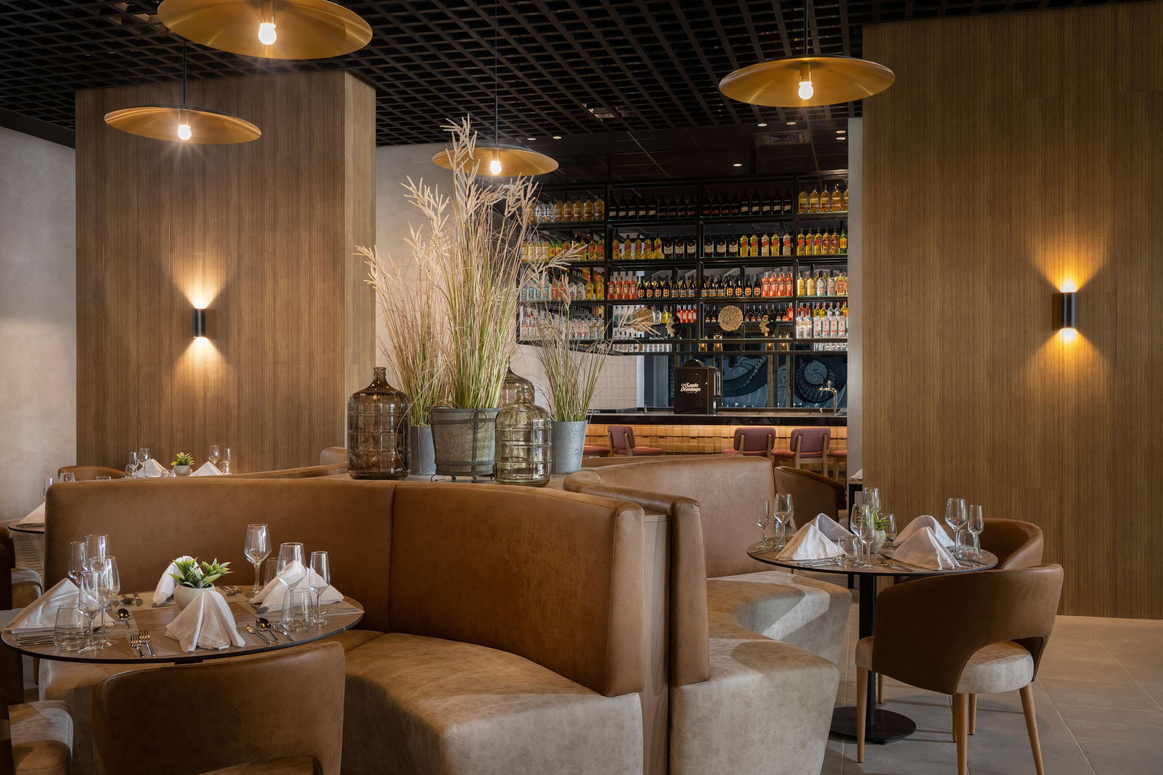A restaurant with leather booths, round tables, and a bar area in the background.
