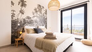 Un dormitorio con una cama grande, una mesita de noche, una lámpara, un mural en la pared y un balcón con vistas.
