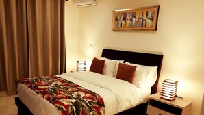 Un letto rifatto con cura, con copriletto floreale, una testiera, due comodini con lampade e un quadro appeso al muro.