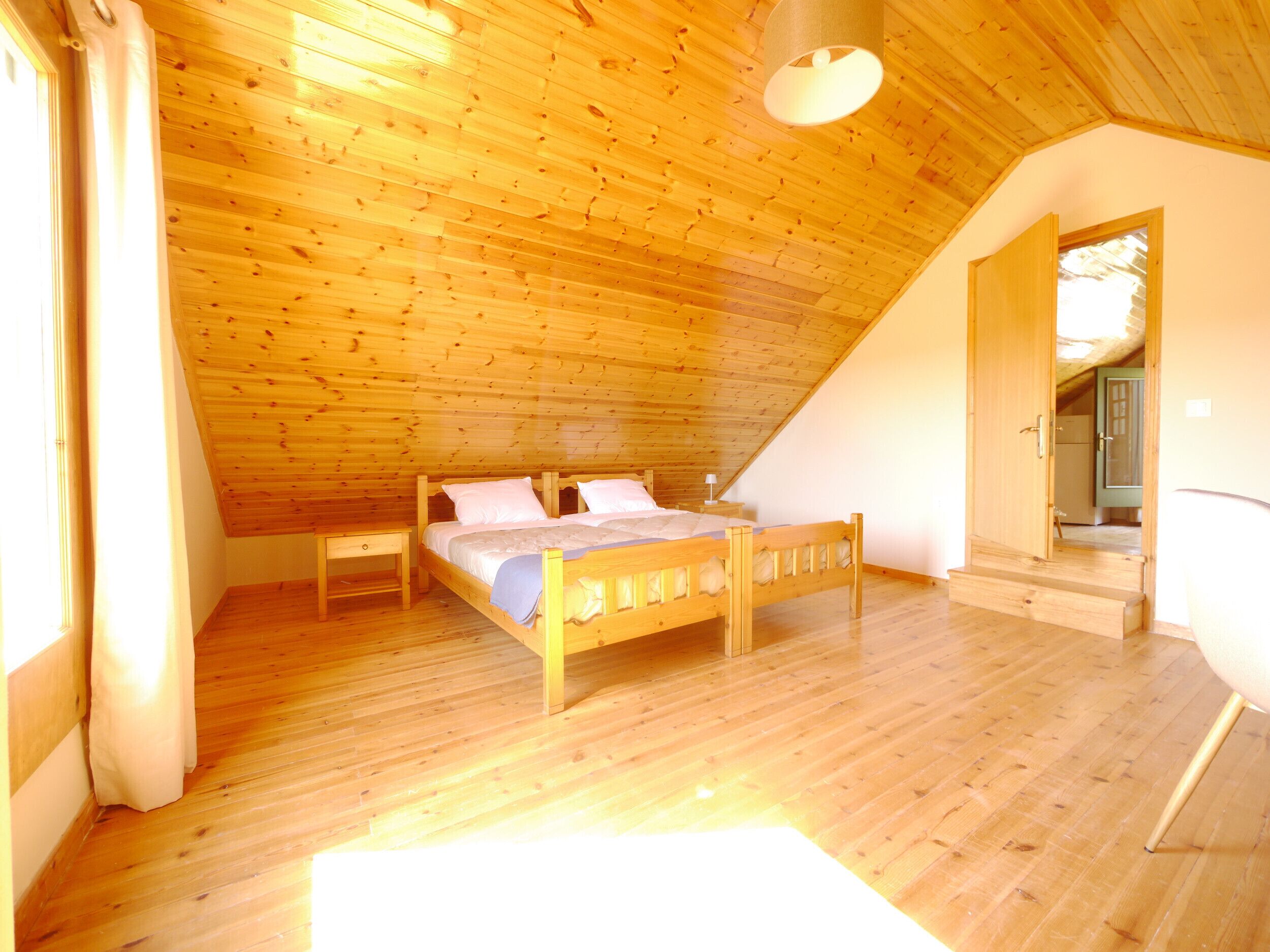 A bedroom with a wooden ceiling, a bed, a nightstand, and a door leading to another room.