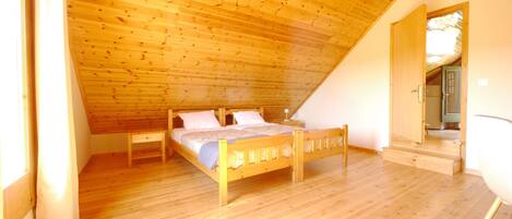 A bedroom with a wooden ceiling, a bed, a nightstand, and a door leading to another room.