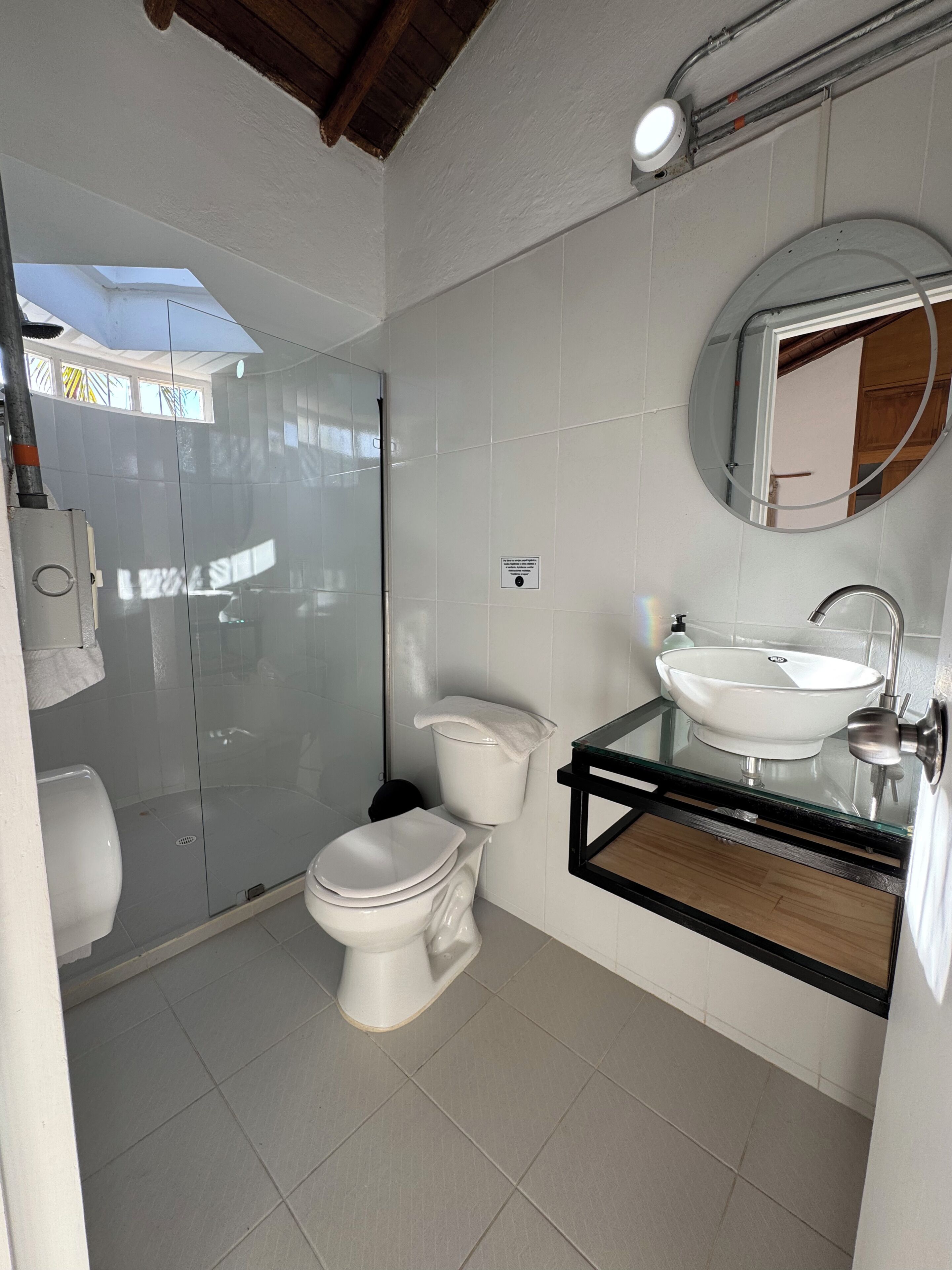 Ein modernes Badezimmer mit einer gläsernen Duschkabine, einer weißen Toilette und einem Waschbecken aus Glas mit Holzablage.