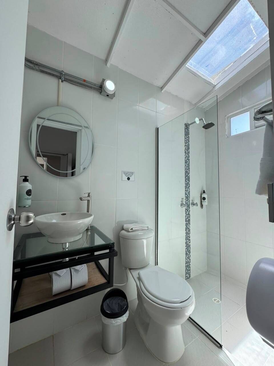 Un baño moderno con cabina de ducha de vidrio, inodoro blanco y lavamanos de vidrio sobre encimera negra.