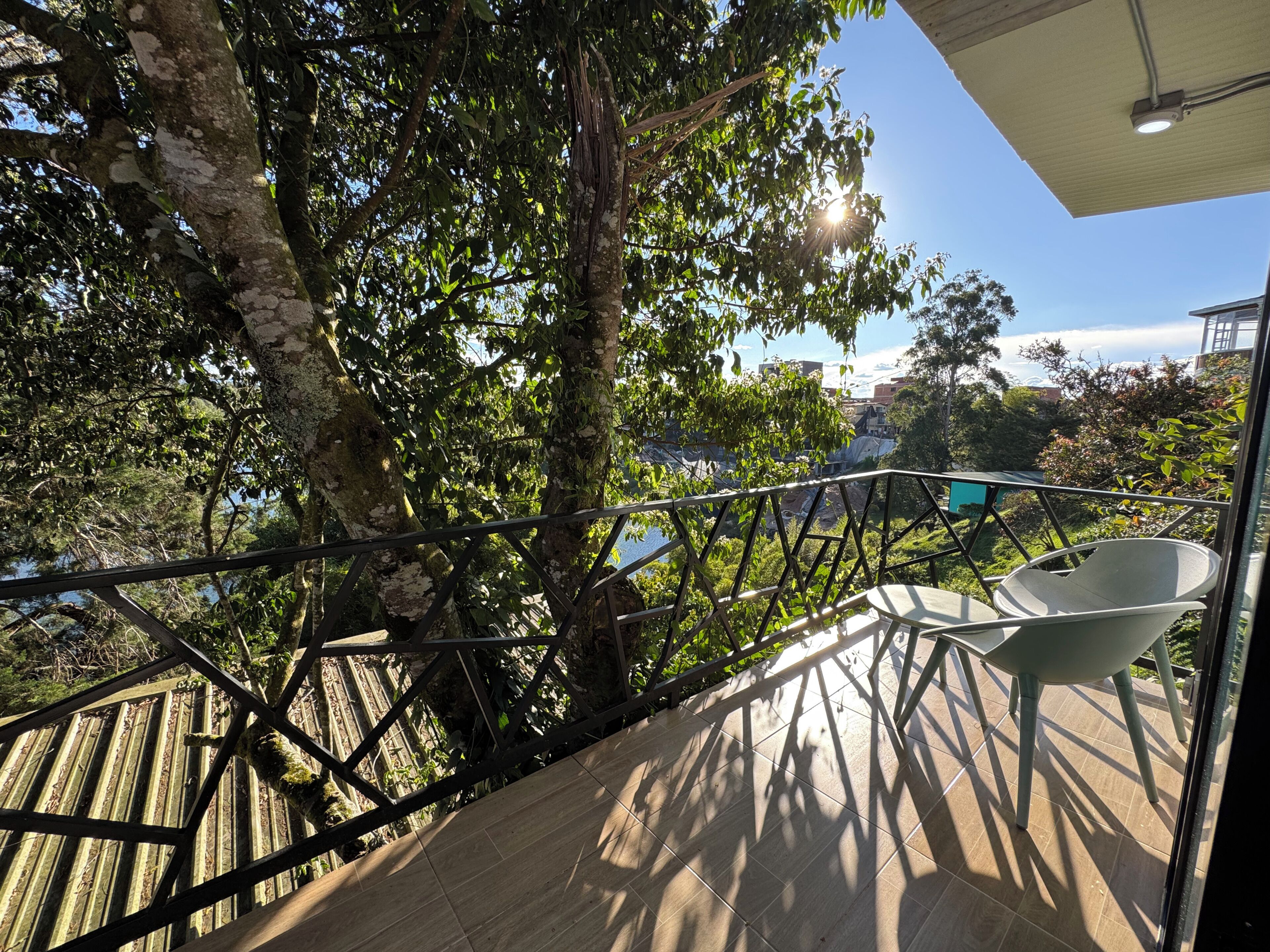 A balcony with a metal railing, a white chair, and a view of trees and buildings.