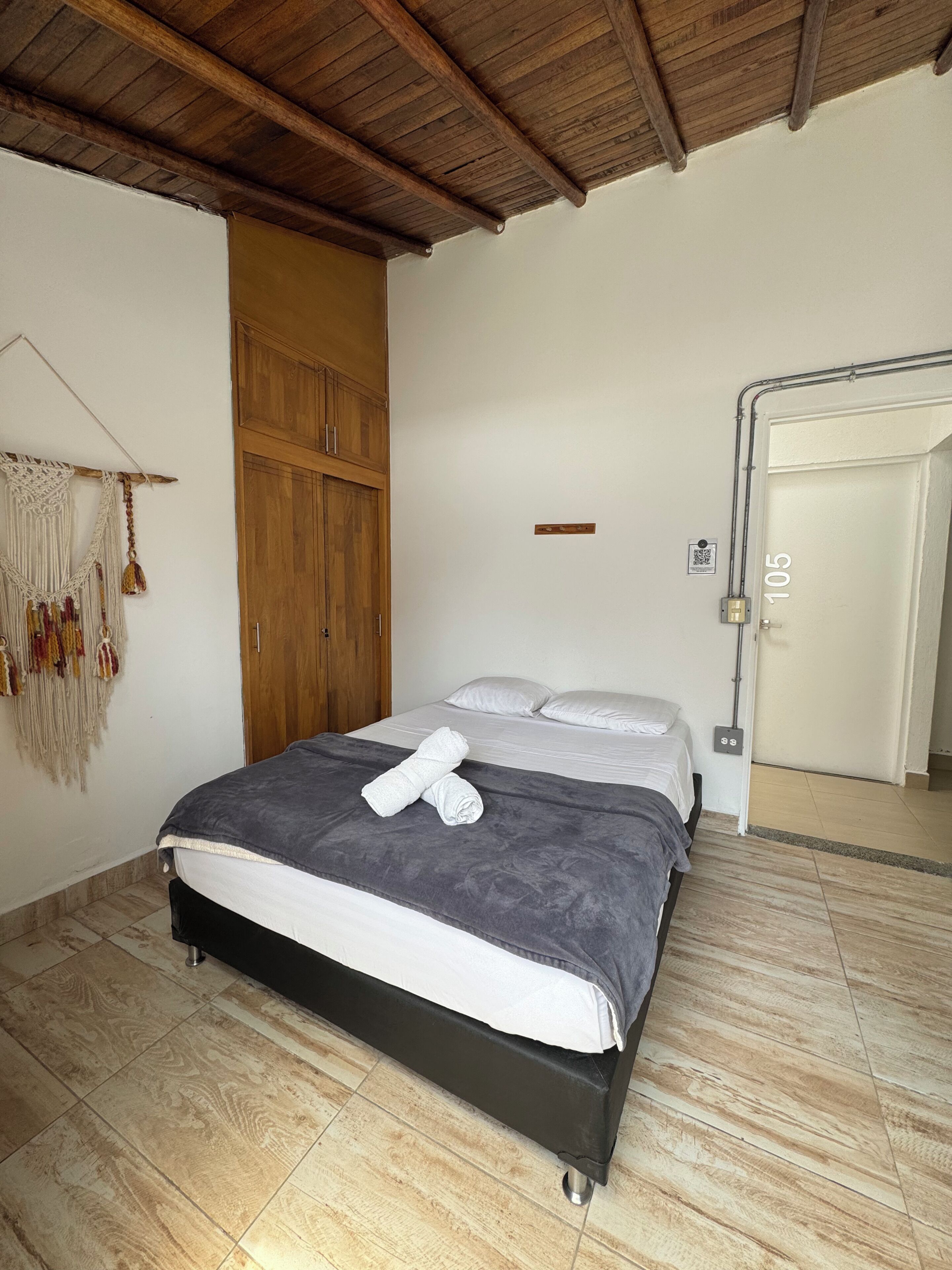 A bedroom with a bed, wooden wardrobe, and a macrame wall hanging.