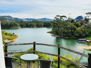 Una terrazza con tavolo e sedie affacciata su un lago, circondata da vegetazione e montagne.