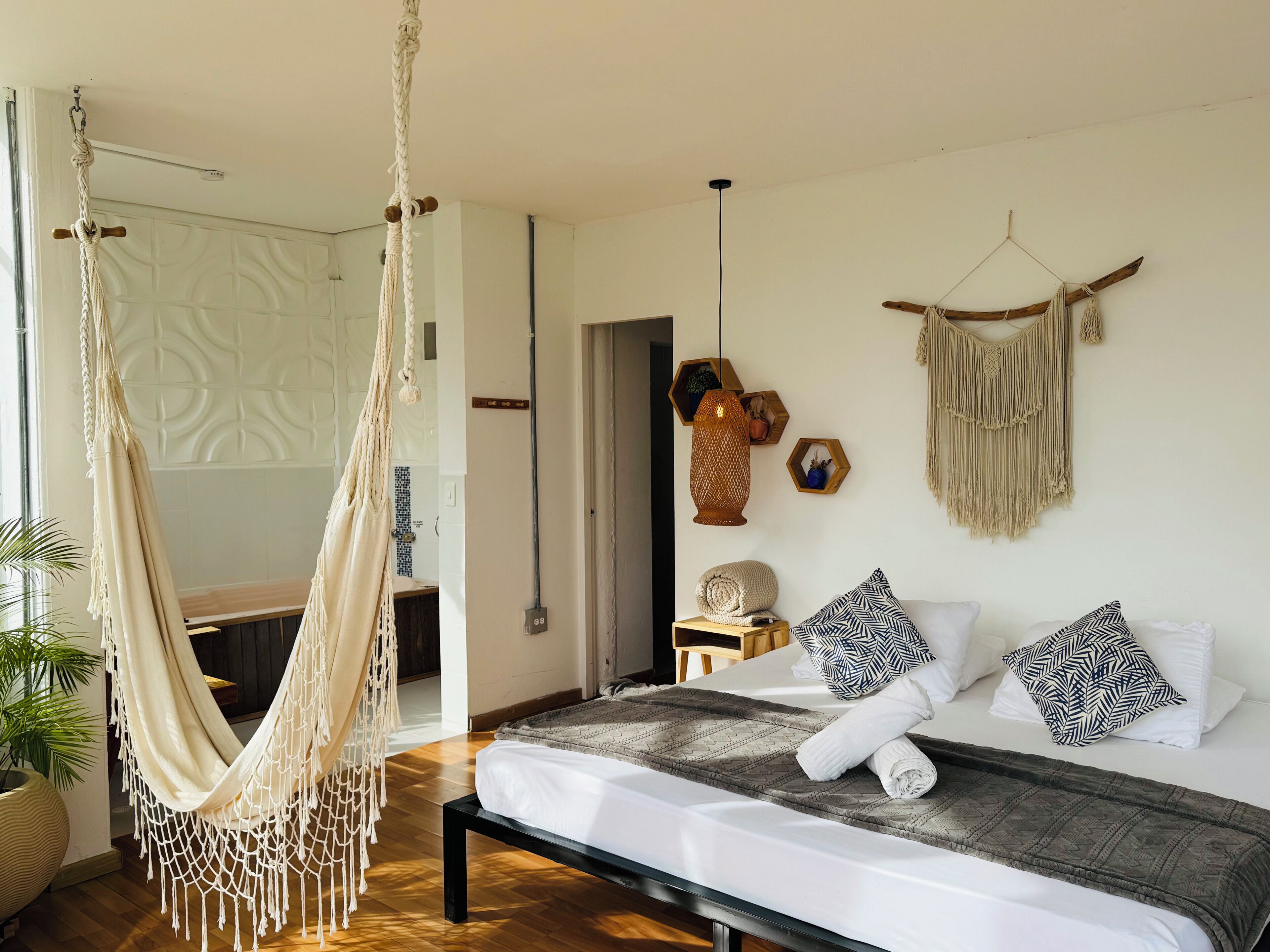 A room with a bed, a hammock, a macrame wall hanging, and a wooden bench.