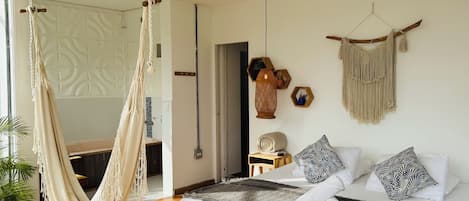 A room with a bed, a hammock, a macrame wall hanging, and a wooden bench.