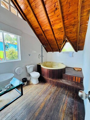 Un bagno con soffitto in legno, una vasca, un water e una finestra.