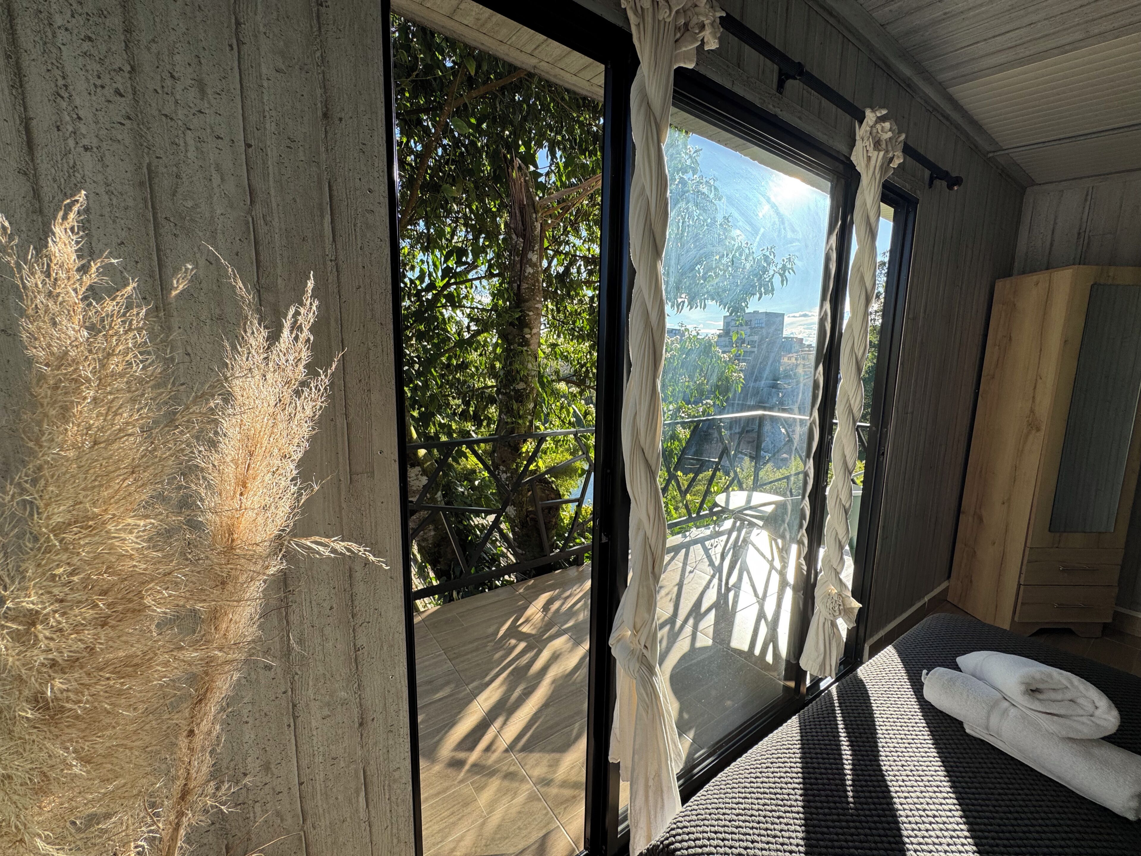 Ein Zimmer mit großem Fenster, einem Bett mit dunkel strukturiertem Überwurf und einem Holzschrank.