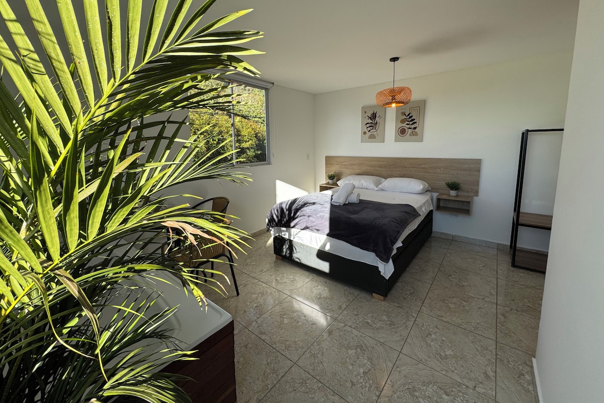 A bedroom with a bed, a window, a plant, and a hanging light fixture.
