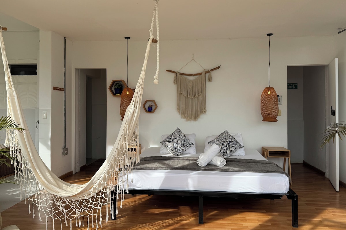 A bedroom with a bed, macramé hanging decorations, and a hammock.