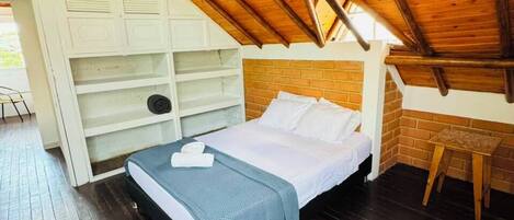 A bedroom with a sloped ceiling, a bed, a wooden floor, and built-in shelving.