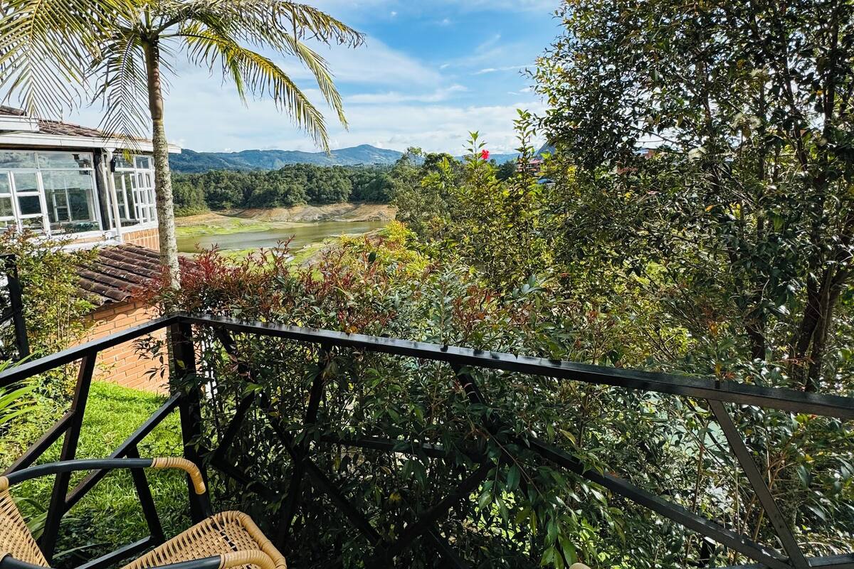 A covered balcony with wicker chairs, a view of a river, and surrounding greenery.