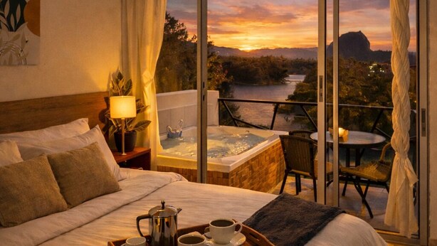 A hotel room with a large bed, a hot tub, a dining area with a table and chairs, and a view of a sunset over a body of water. - La Madriguera Hotel Guatapé Con Embalse (Guatapé)