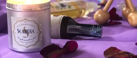 A candle labeled 'Scandle' on a purple surface with rose petals and wooden objects.