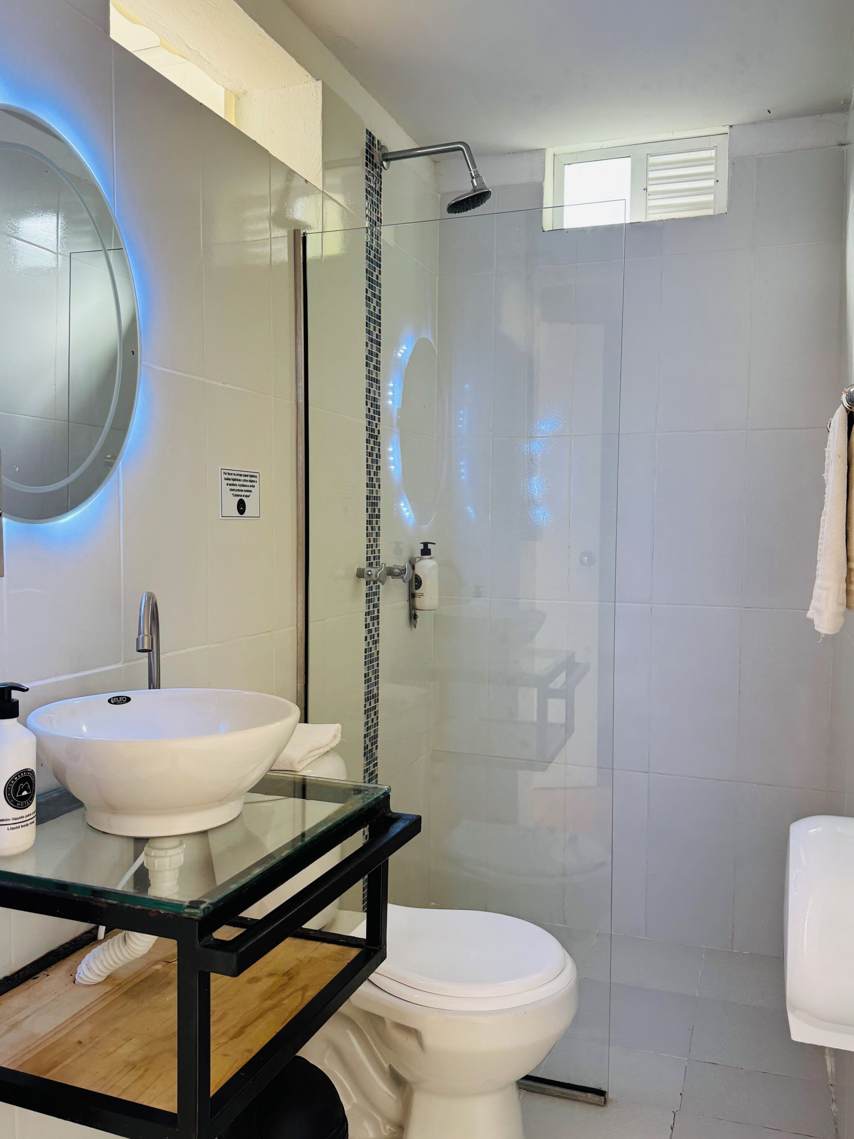 A modern bathroom with a glass-enclosed shower, a white sink with a glass top, and a toilet.