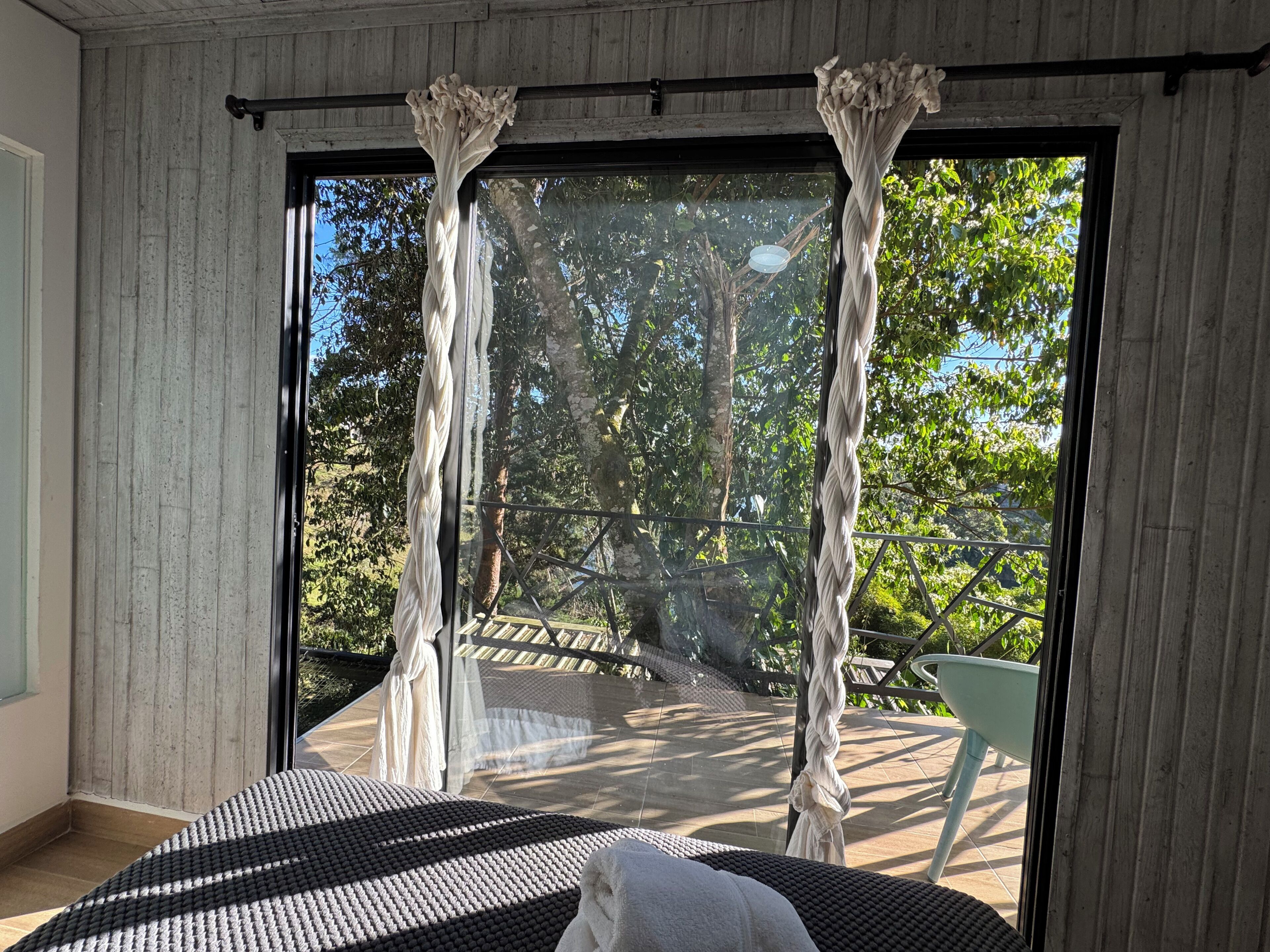 Et værelse med en seng, et vindue med gardiner og udsigt til en balkon med gelænder.