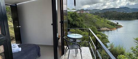 Un balcón con una cama, una mesa y sillas, con vistas a un lago y un paisaje montañoso.