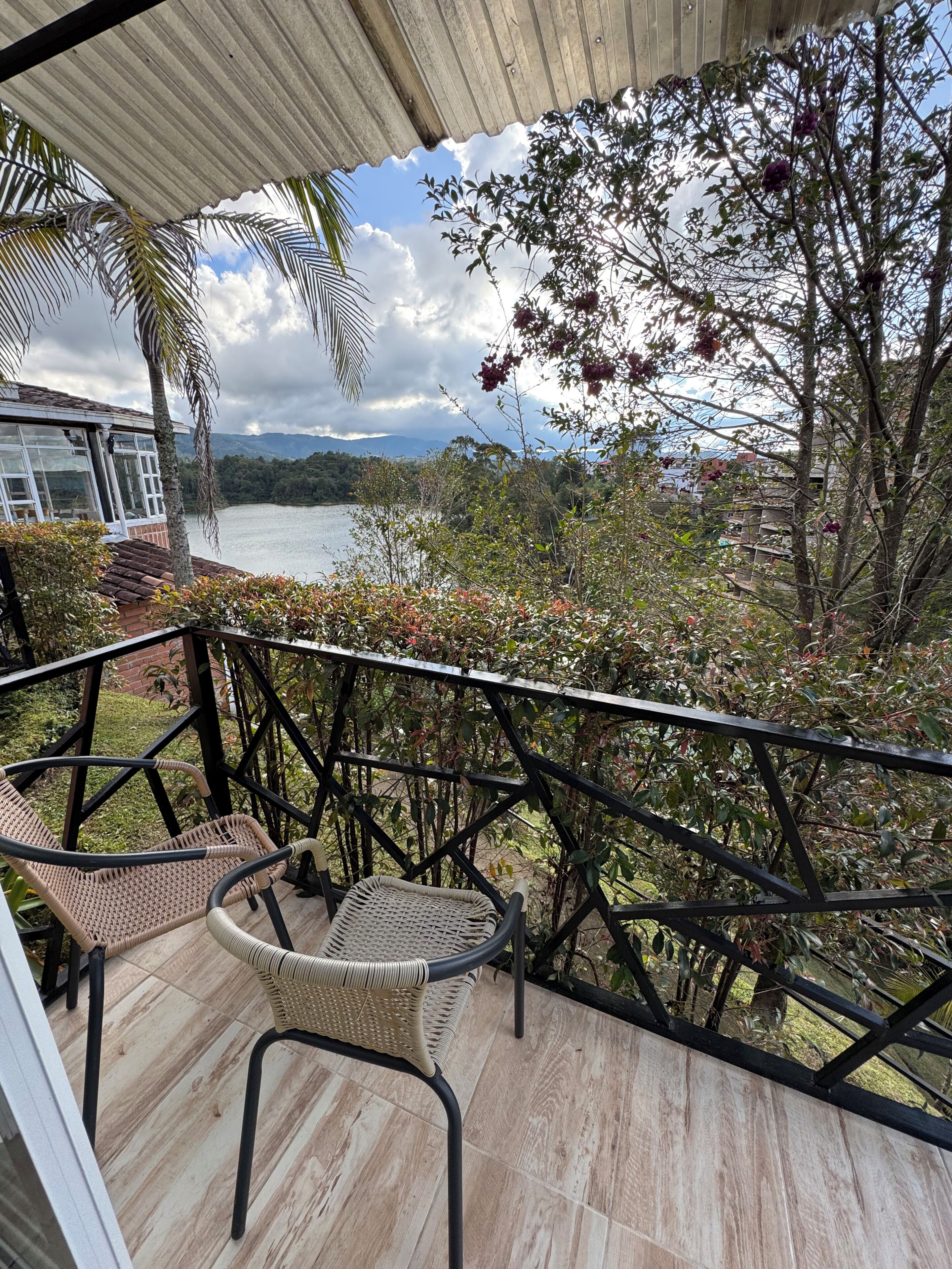 A balcony with wicker chairs, a view of a lake, and surrounding vegetation.