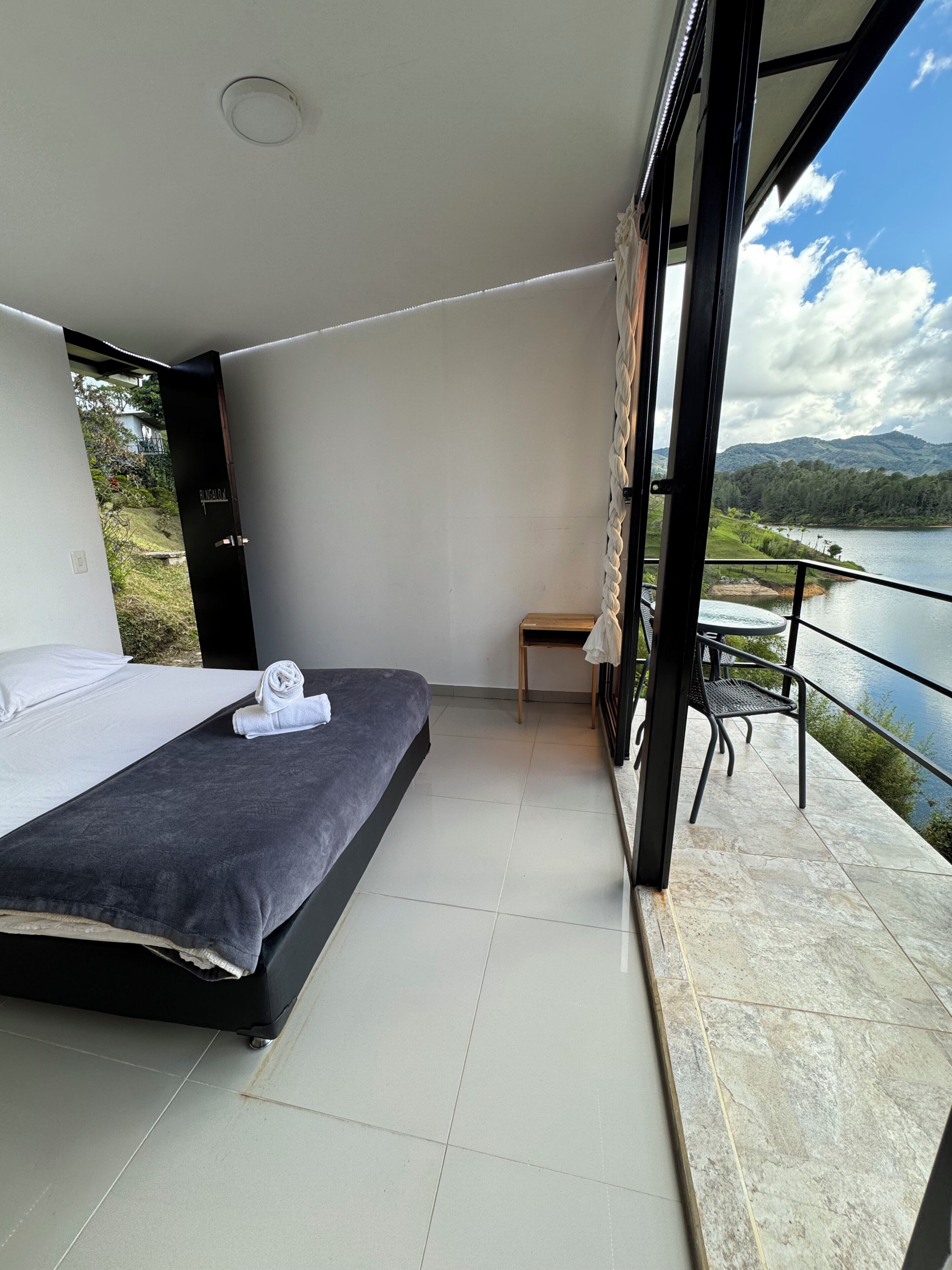 A bedroom with a bed, a small table, and a view of a lake and mountains.