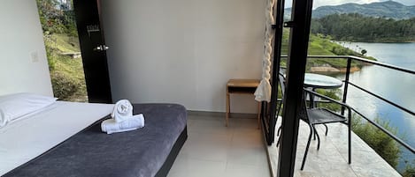 A bedroom with a bed, a small table, and a view of a lake and mountains.